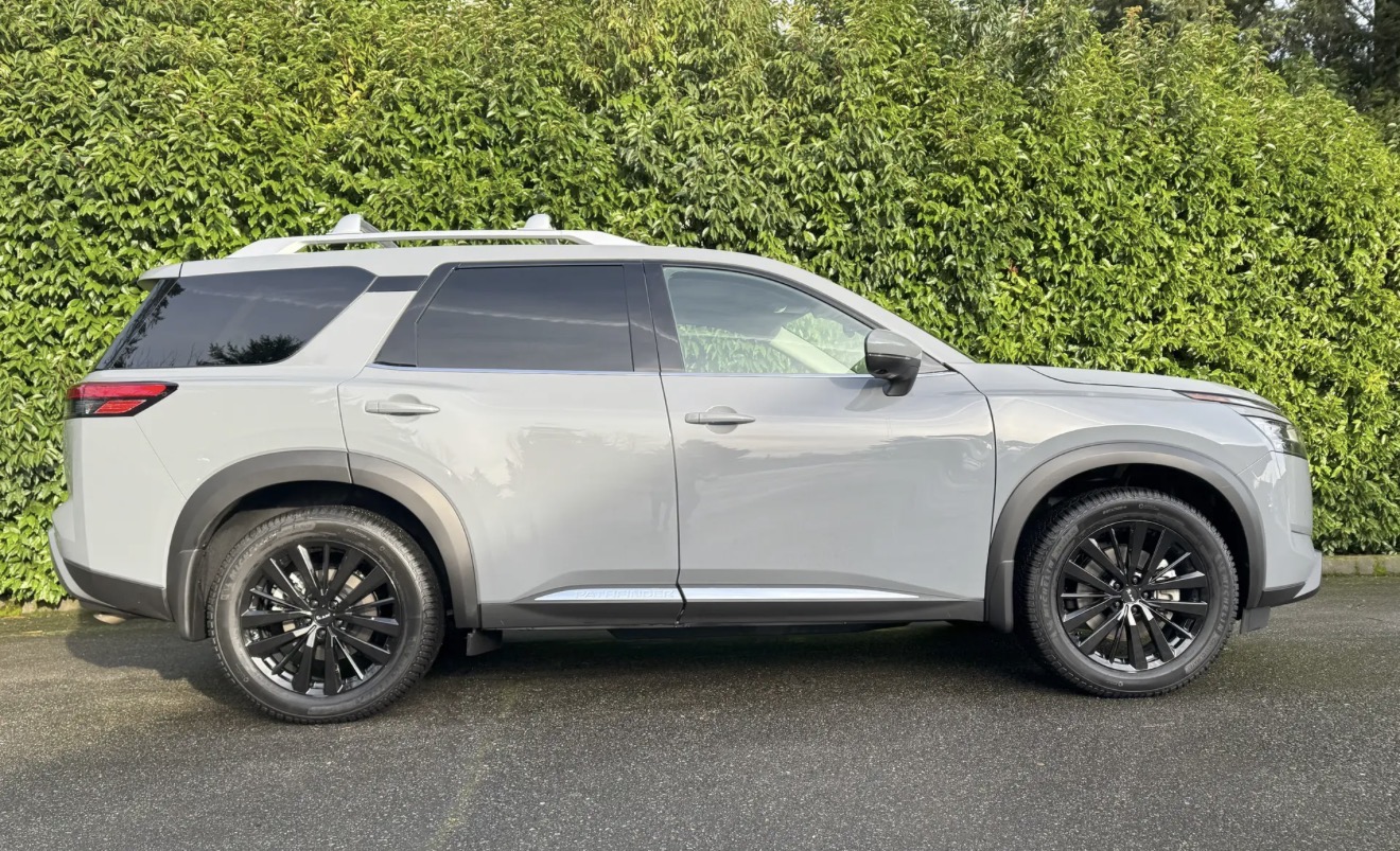 Silver Nissan Pathfinder SUV detailed, side profile against green hedge